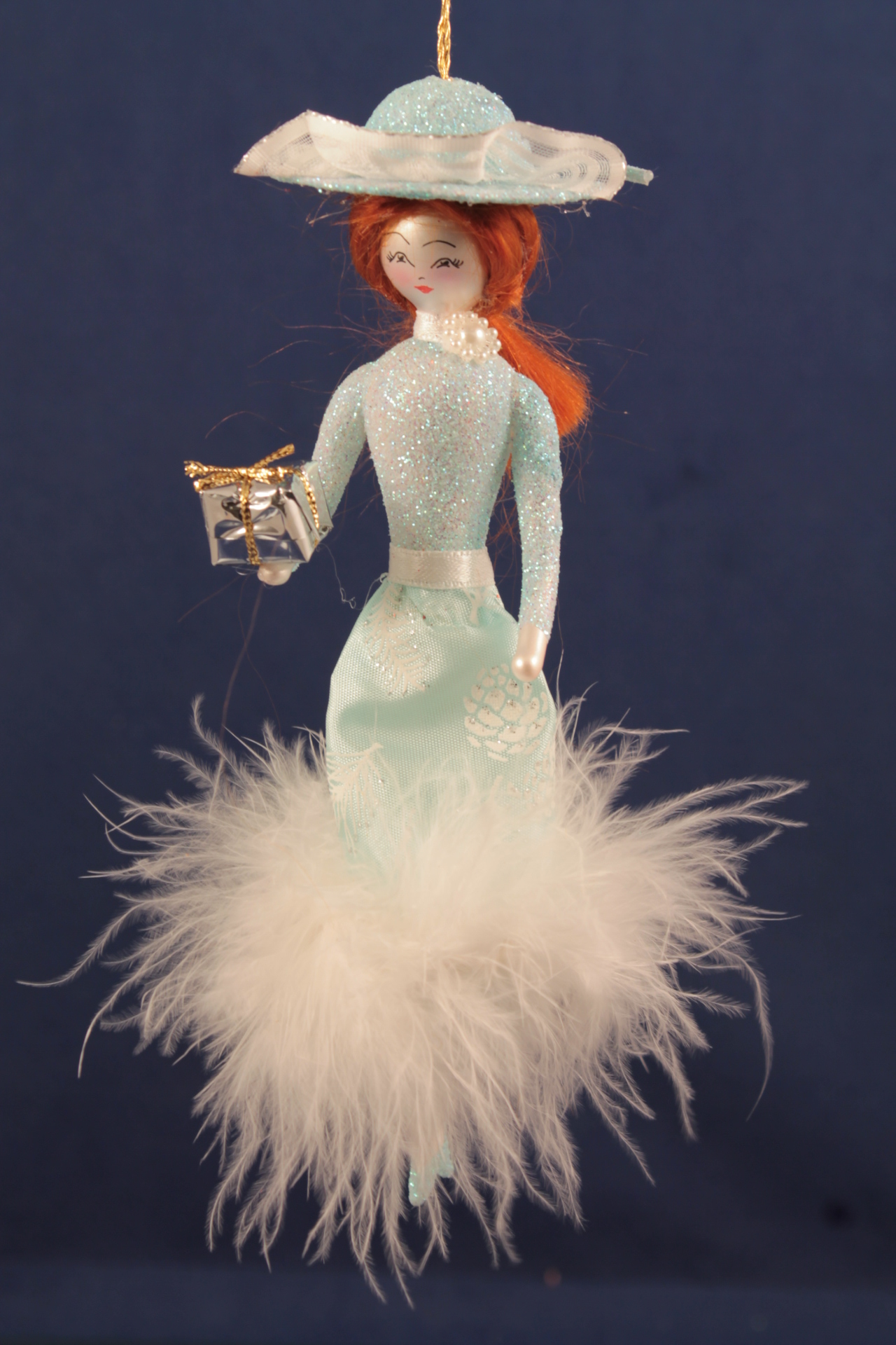 Новогодняя игрушка в виде девушки с подарком, одетой в блестящее платье с перьями и шляпу.